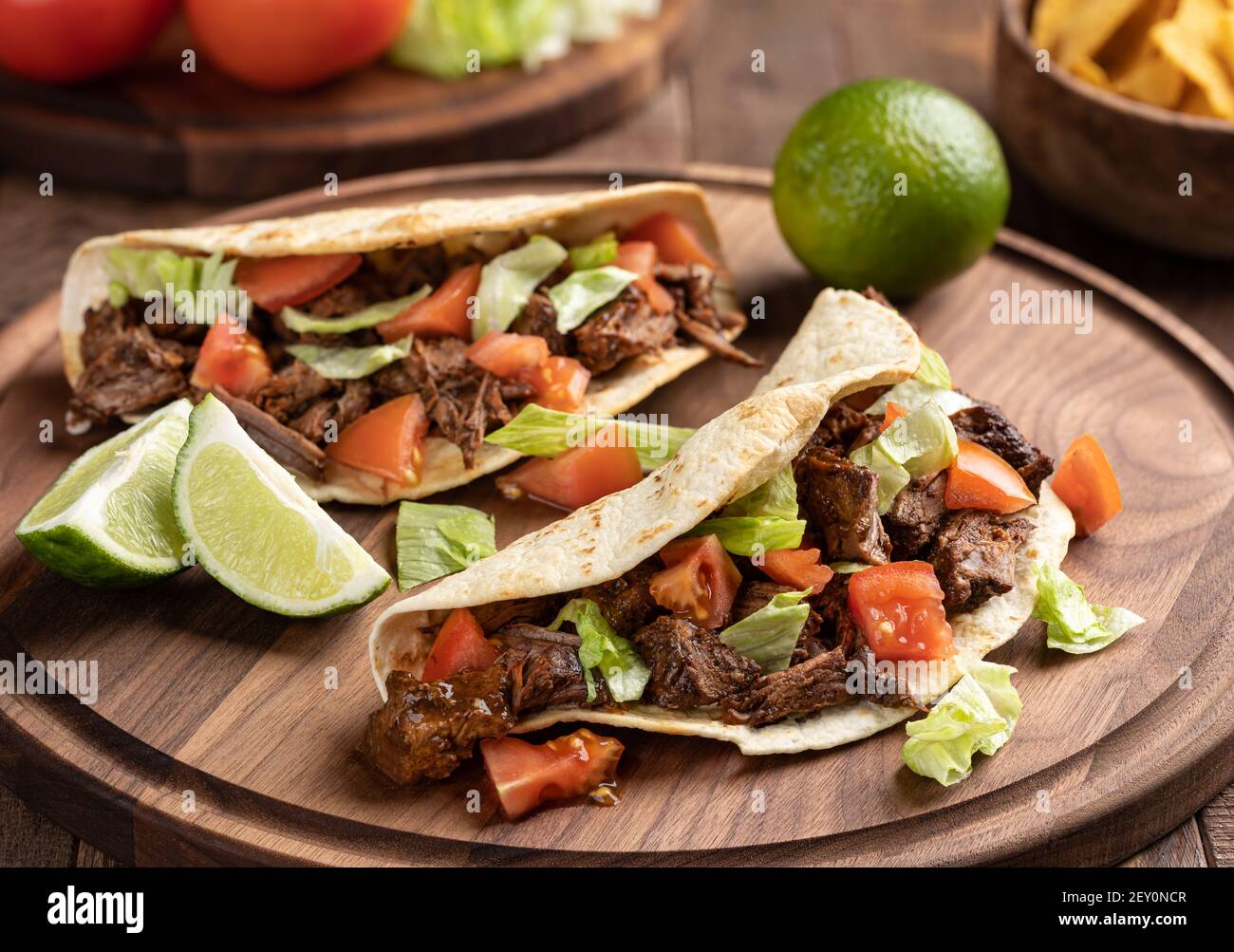 Tacos made with roast beef, lettuce and tomato on a tortilla shell on a wooden platter Stock