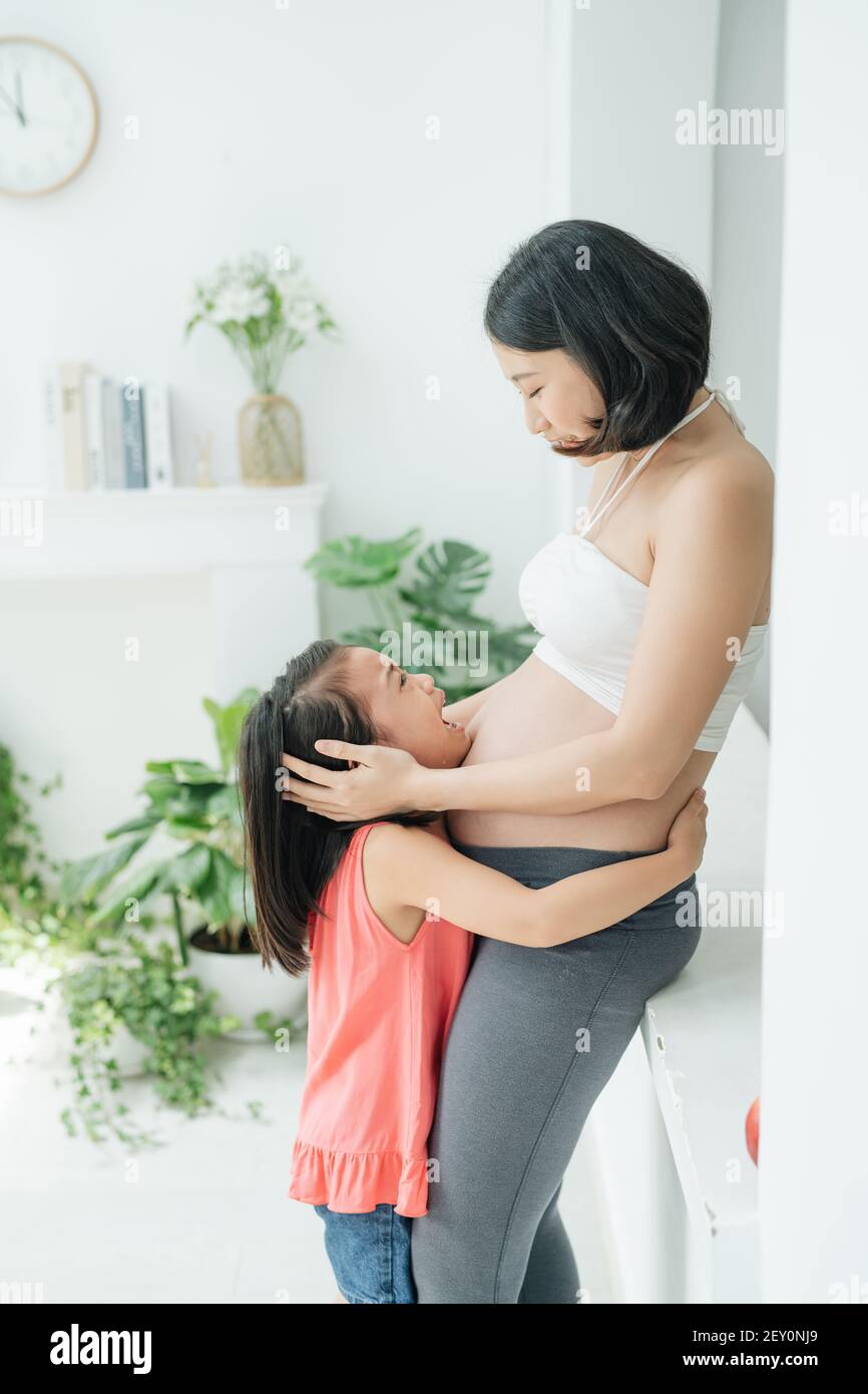 I don't want brother. Sad little daughter looking at her pregnant mom belly, child crying for not wanting sibling, family issue, close up Stock Photo