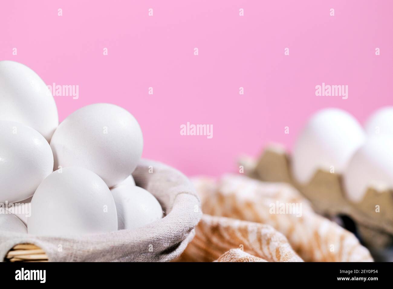 White Chicken eggs in a cardboard box and in a Straw basket on a pink background with piece of cloth, Raw Fresh Chicken Eggs in a paper container Stock Photo