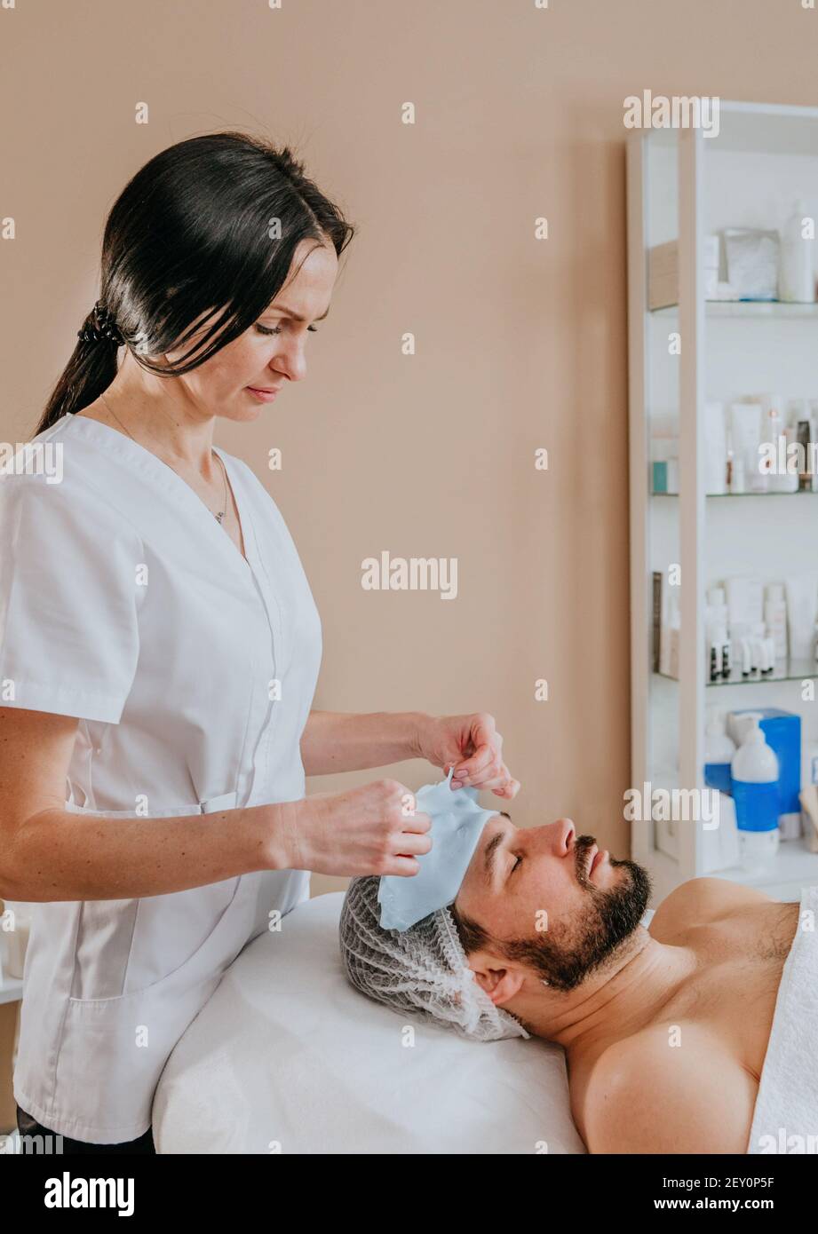 Esthetician making facial cleansing procedure using algae mask for a man Stock Photo
