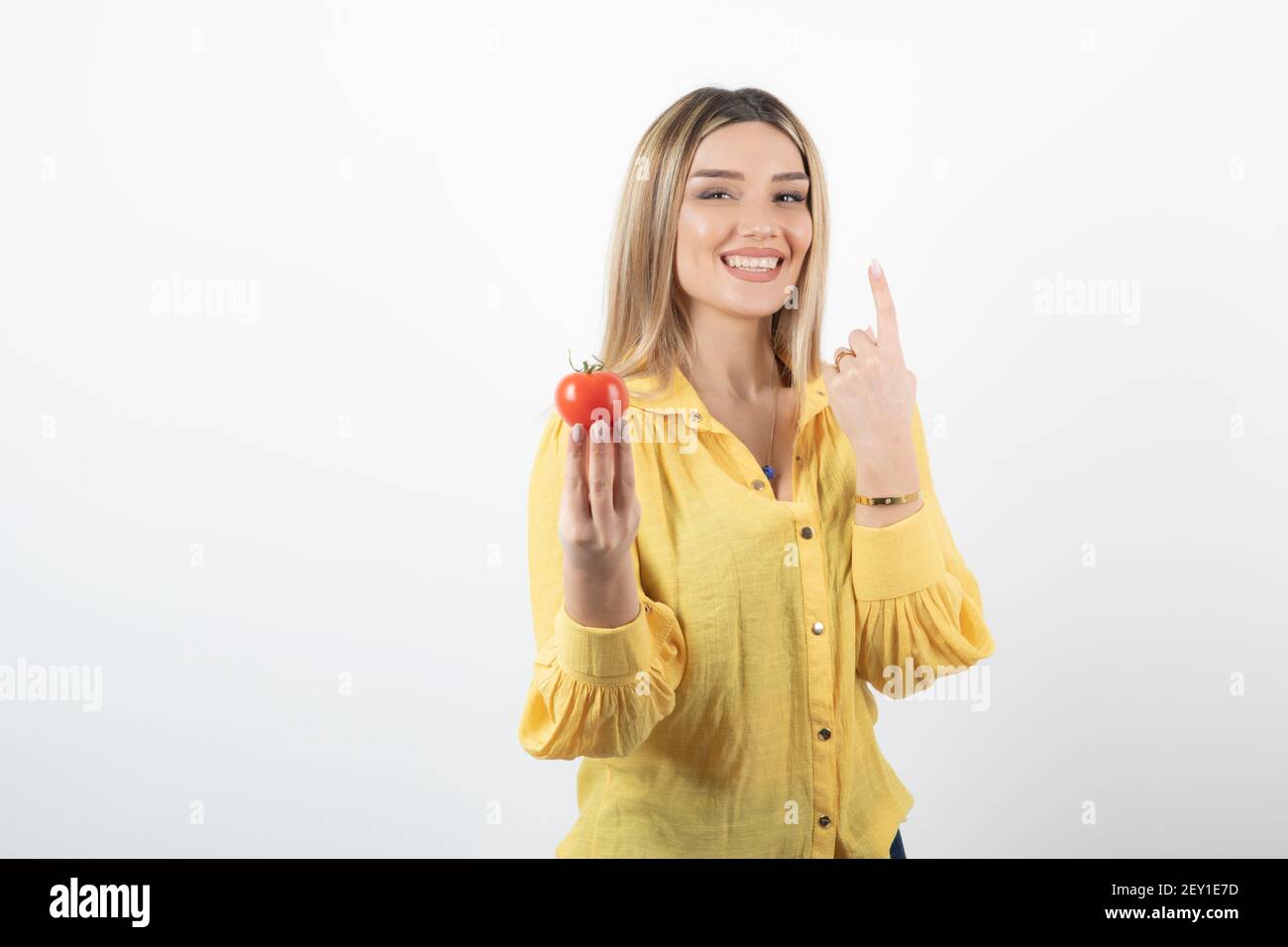Smiling woman holding red tomato an sticking her tongue out on white ...