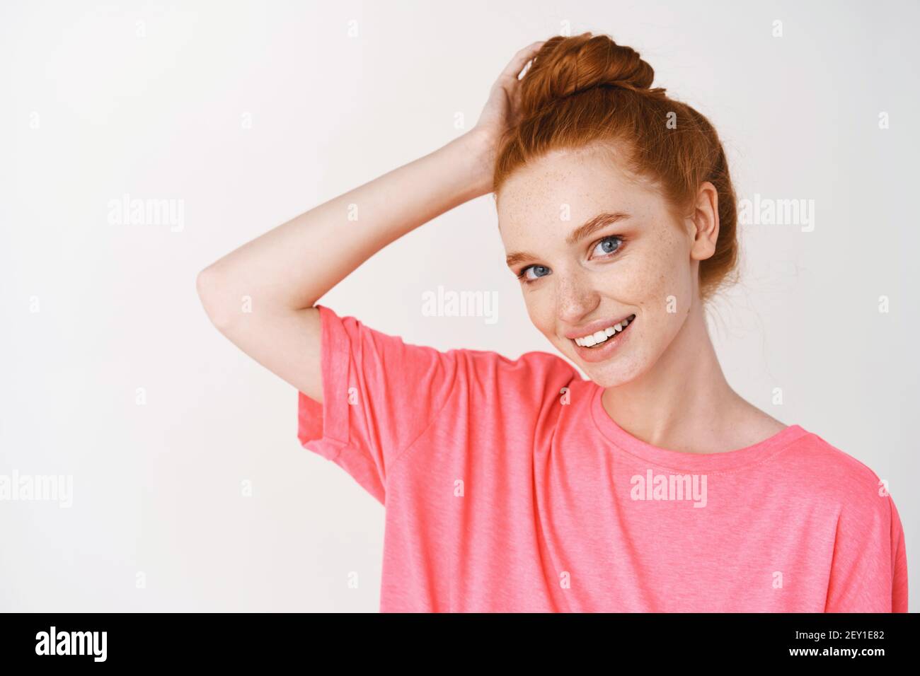 Beauty and skincare. Young woman with red hair combed in messy bun smiling cute at camera, showing healthy glowing skin without acne and blemishes Stock Photo