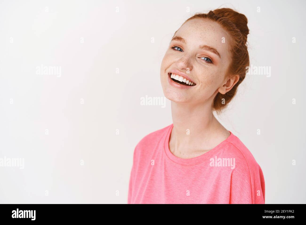 Skincare and makeup concept. Happy young woman with ginger hair combed in messy bun, natural makeup and freckles, laughing and showing white teeth Stock Photo