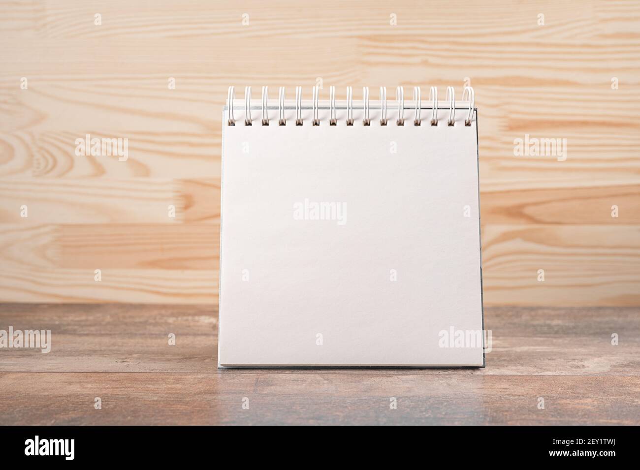 mockup image. square notebook with blank page stands upright on wood table against a wooden wall background. space for your text, message or design. B Stock Photo