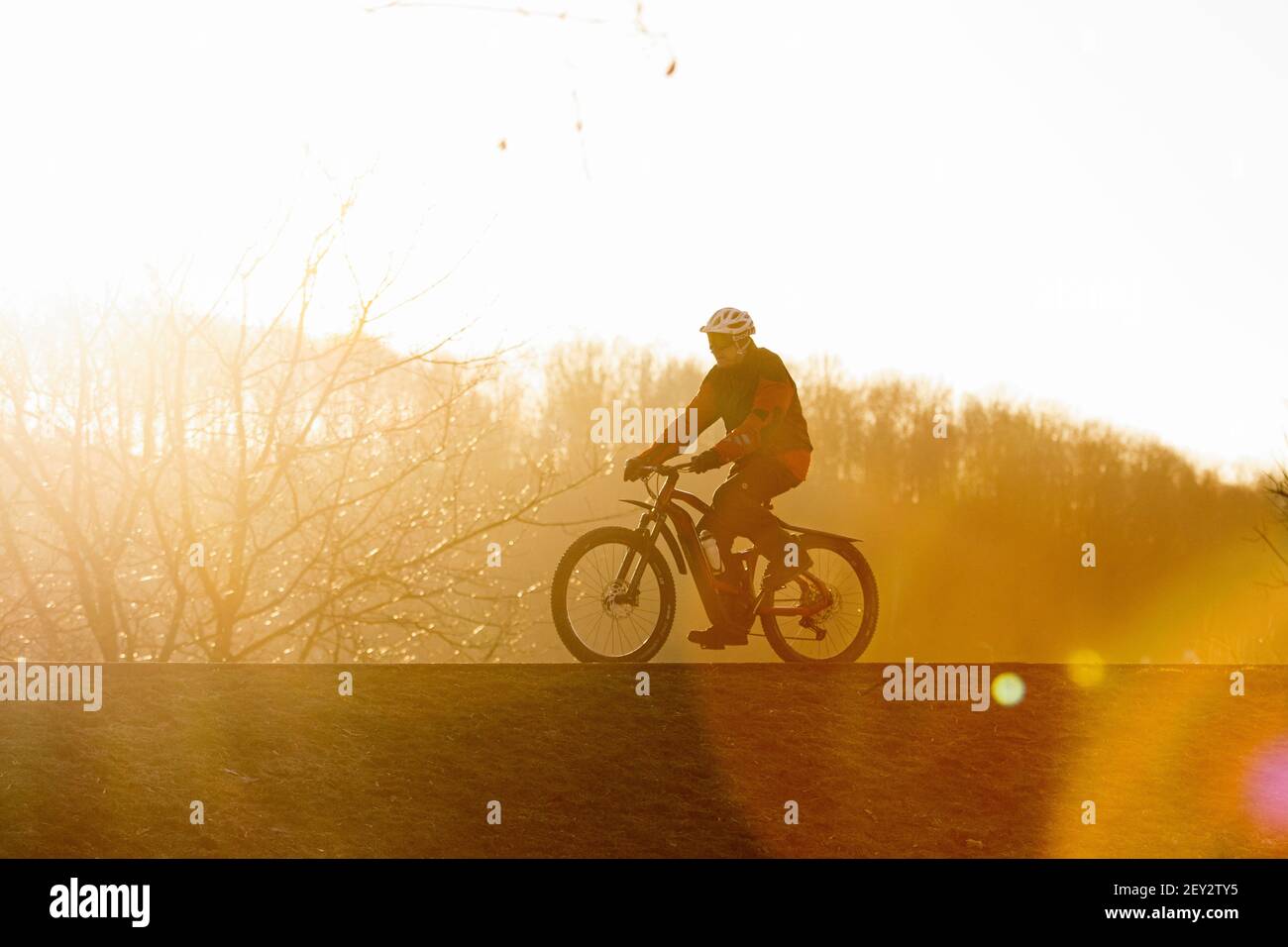 Man rides bicycle in park in amazing sunset behind Stock Photo