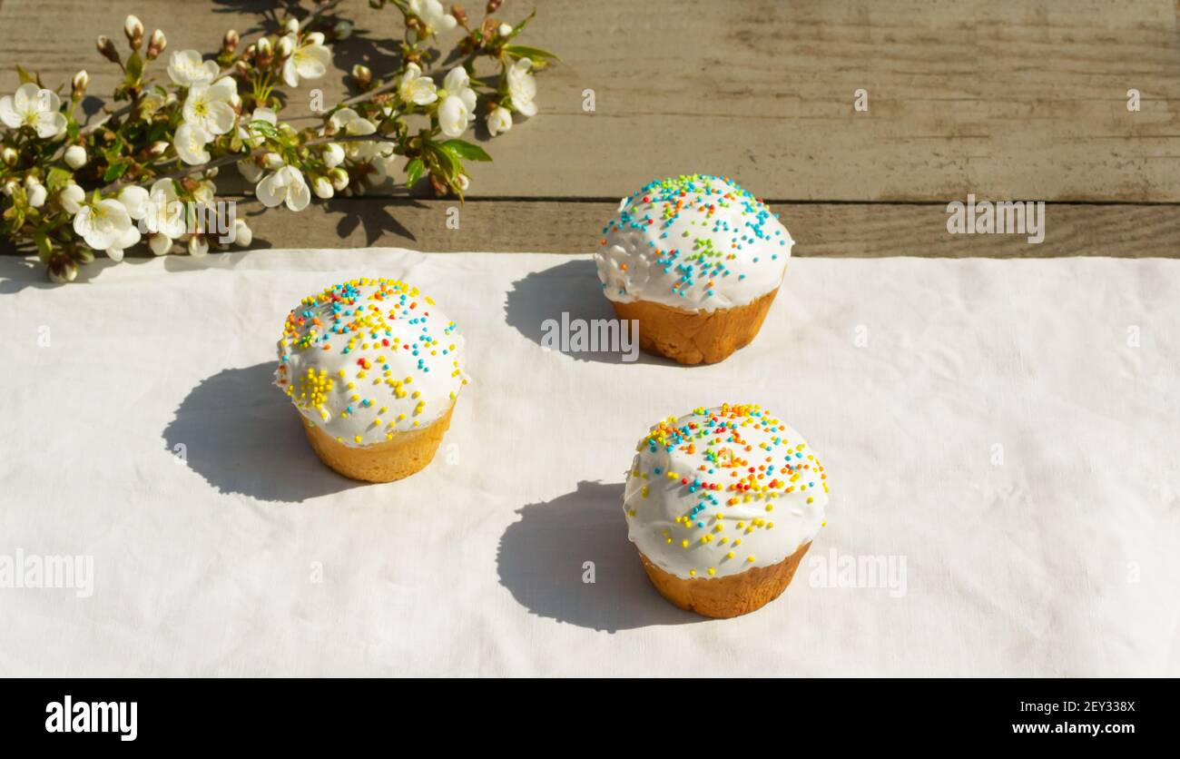 Three Easter cake on a white tablecloth with a branch of a blossoming apple tree. Spring holiday concept. Horizontal orientation. Copy space. Stock Photo