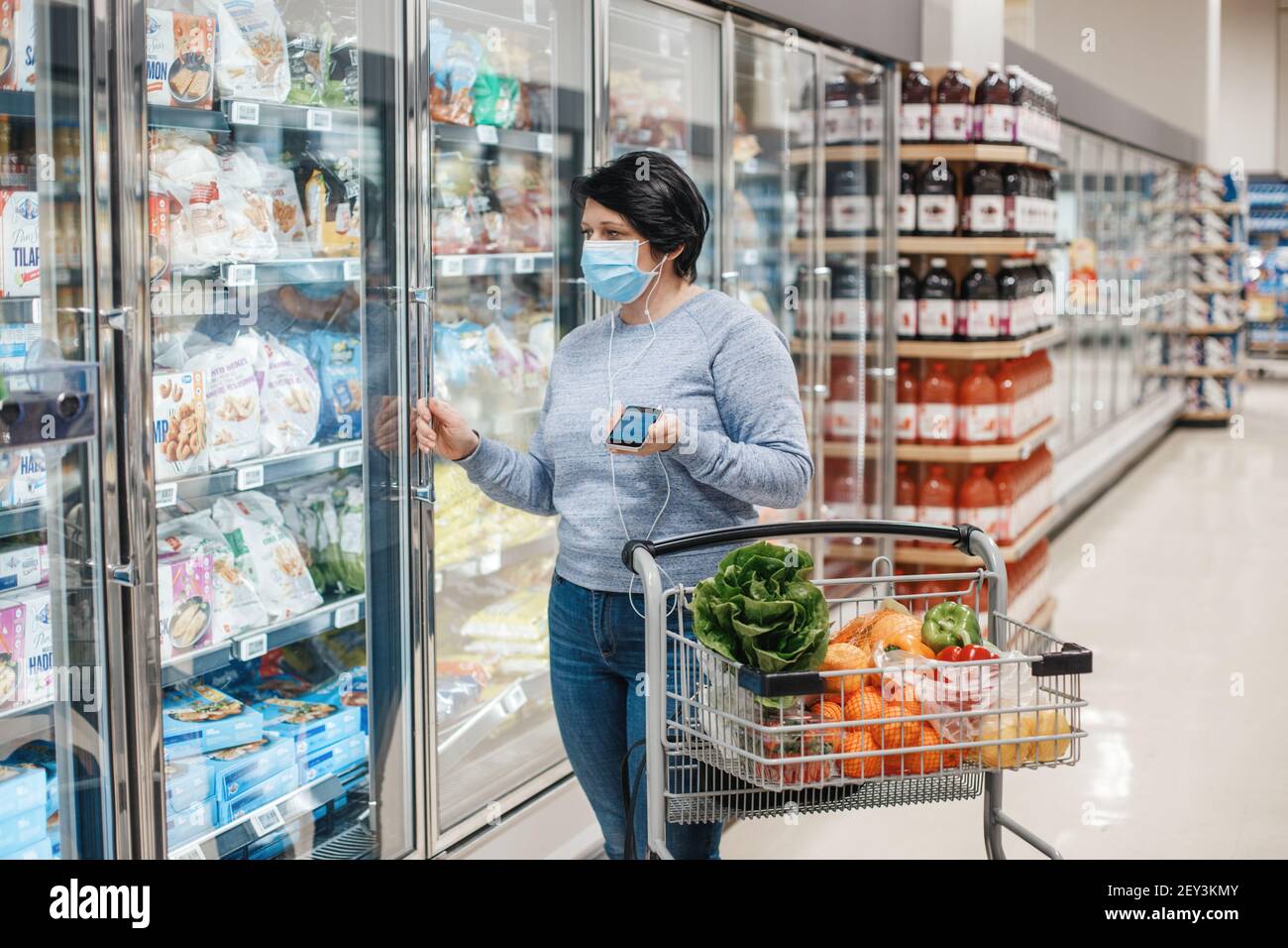 Toronto, Ontario, Canada - February 26, 2021: Middle age brunette woman shopping in grocery store supermarket and talking on audio chat live stream ph Stock Photo