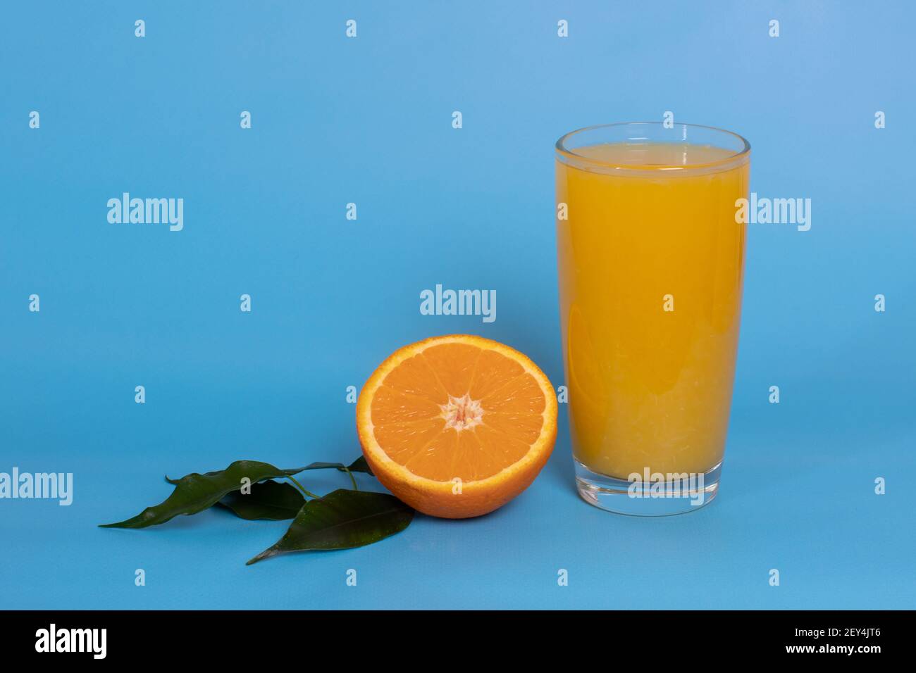 Orange juice in a glass, half an orange with leaves on a blue