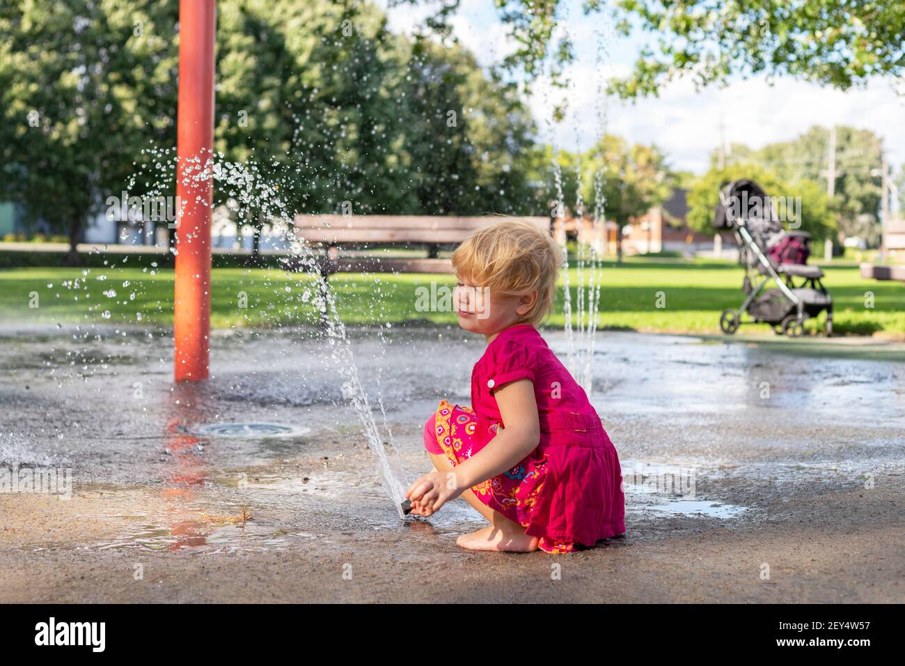 Little girl playing with splash pad water and dirt in the park on sunny day in summer. Stock Photo