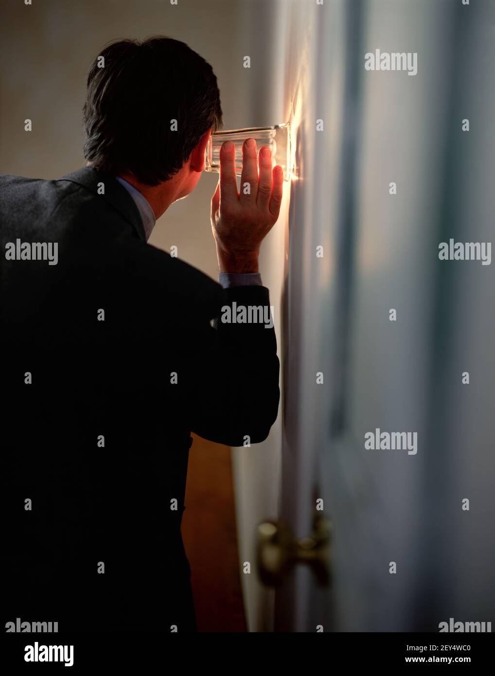 businessman eavesdropping on a conversation in another room by using a glass to amplify the sound Stock Photo