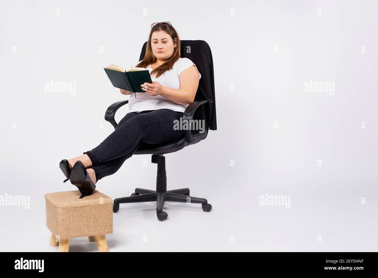 Young overweight woman accountant in glasses working in office, making notes in diary, filing taxes, providing outsource accounting service. Stock Photo