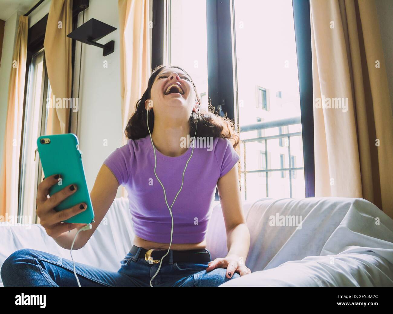happy young woman making video call at home wearing headphones on sofa ...