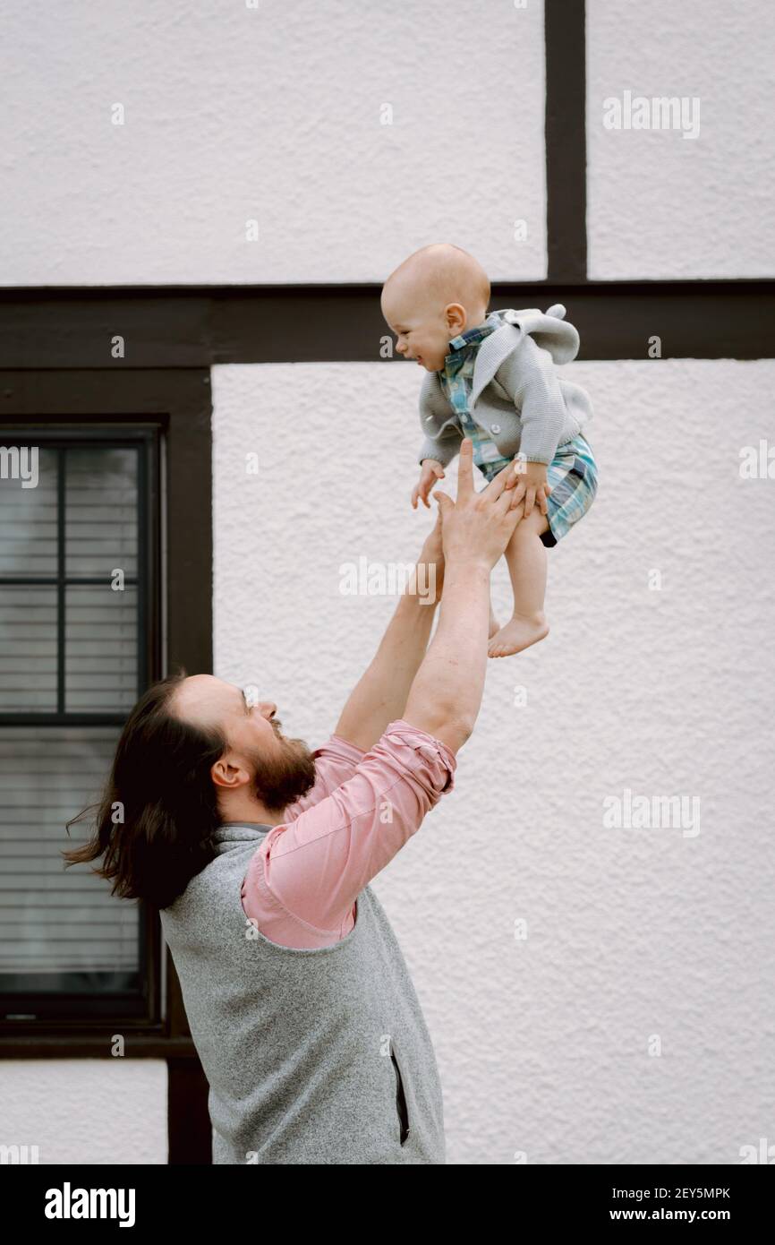 Fun dad throwing laughing baby in front yard in springtime Stock Photo