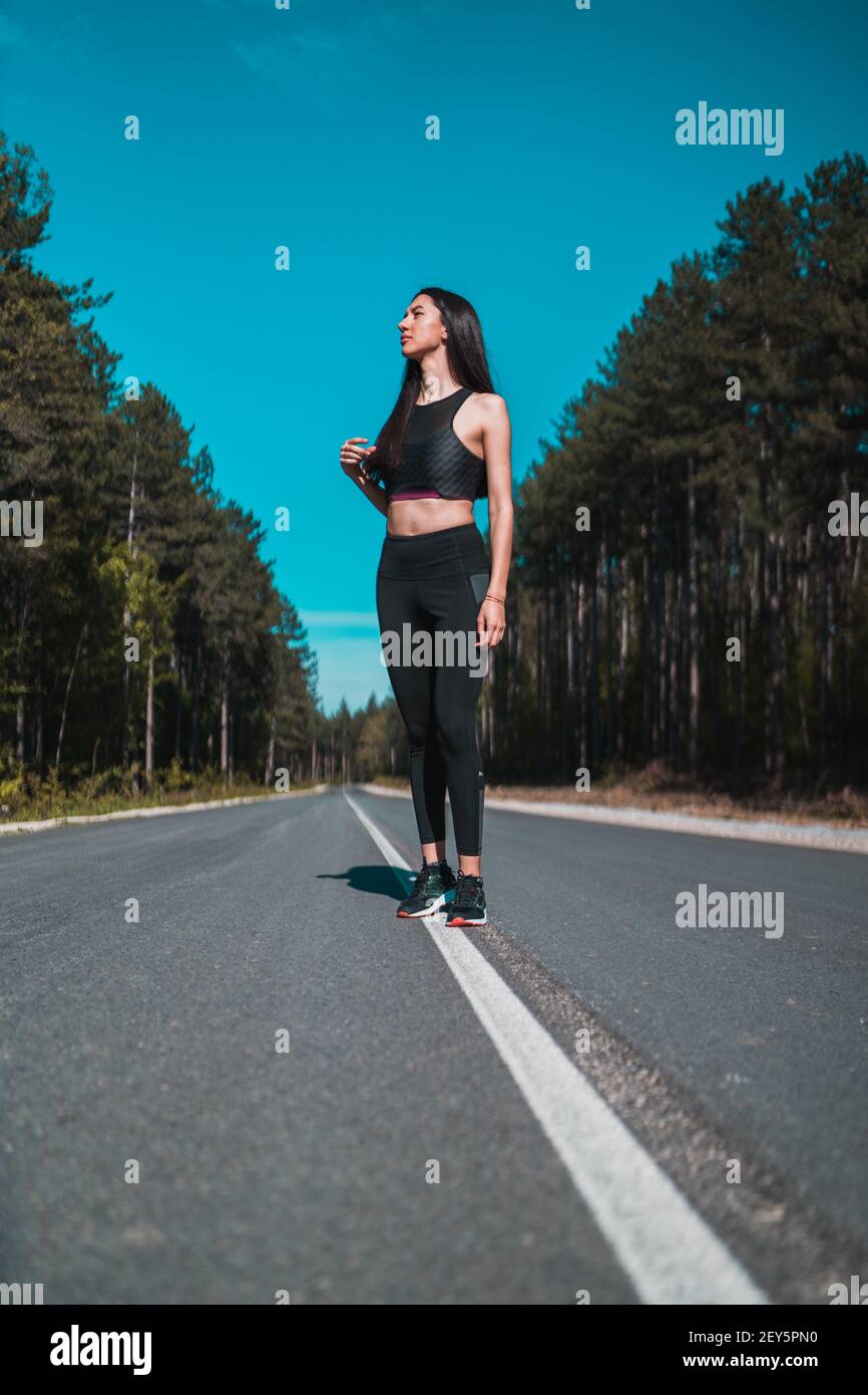 Portrait of Fitness Girl Runner in Black Sporty Top Posing on asphalt road Stock Photo