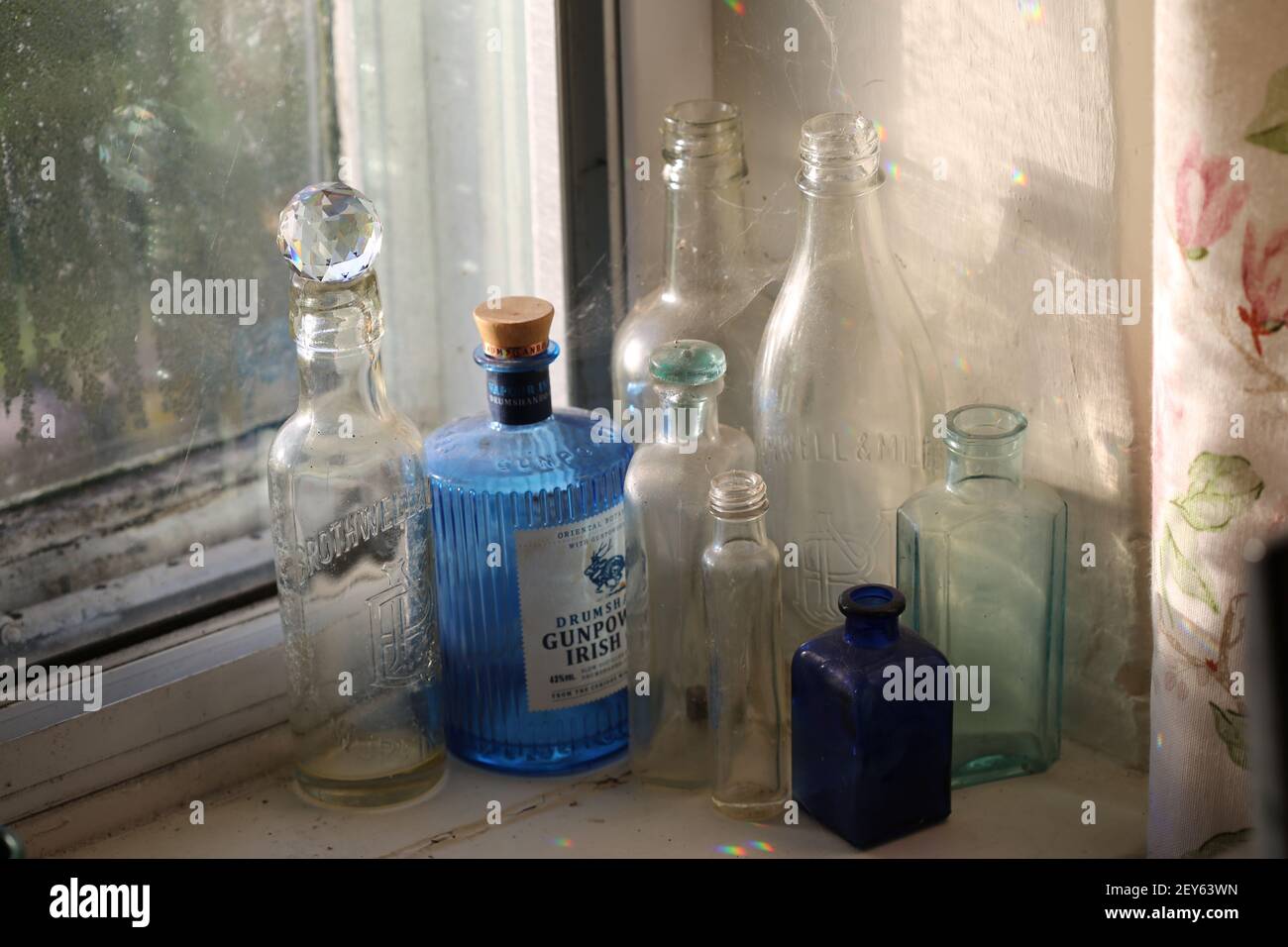Blue and clear vintage bottles in a window with rainbows of light Stock Photo