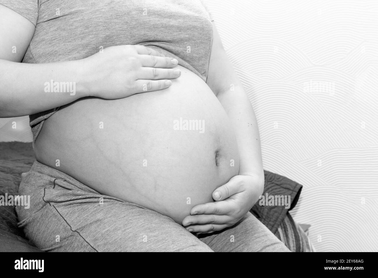 Happy motherhood concept. Female hands hold the belly of a pregnant woman, close-up, black and white. Concept about pregnancy and birth. Stock Photo