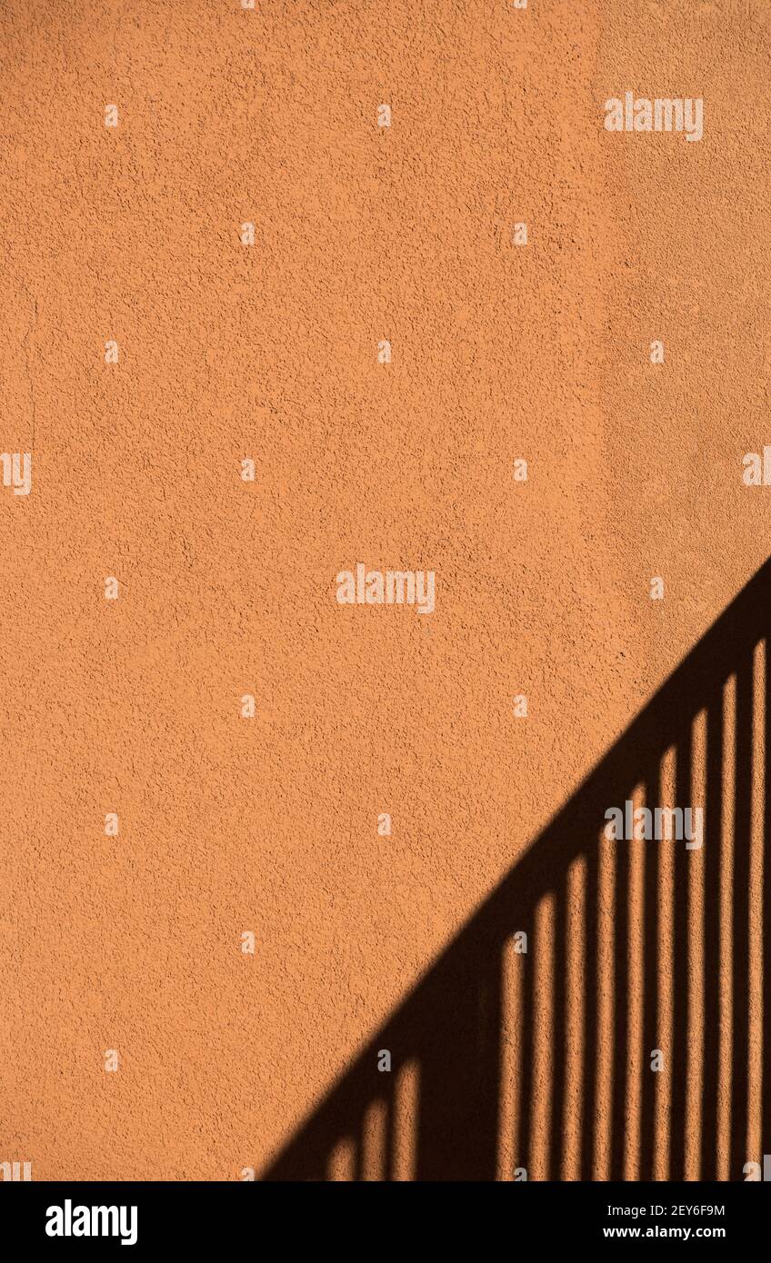 shadow of stair way railing on orange peach colored exterior cement wall of home black lines of stair handle shadow vertical format room for type Stock Photo