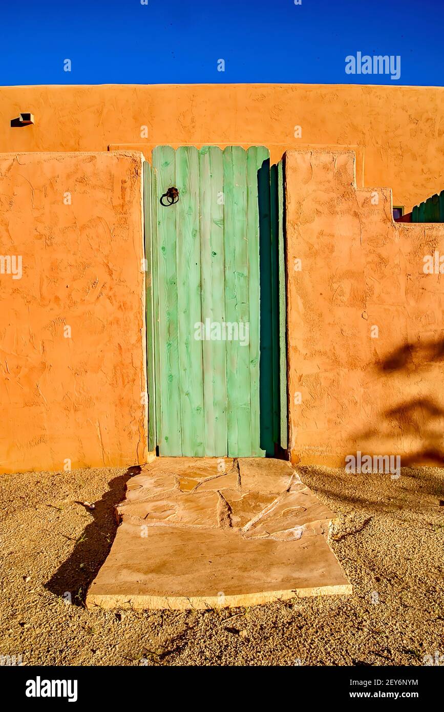 A vertical shot of a bright orange wall with a rustic wooden doorway in Borrego Springs, California Stock Photo