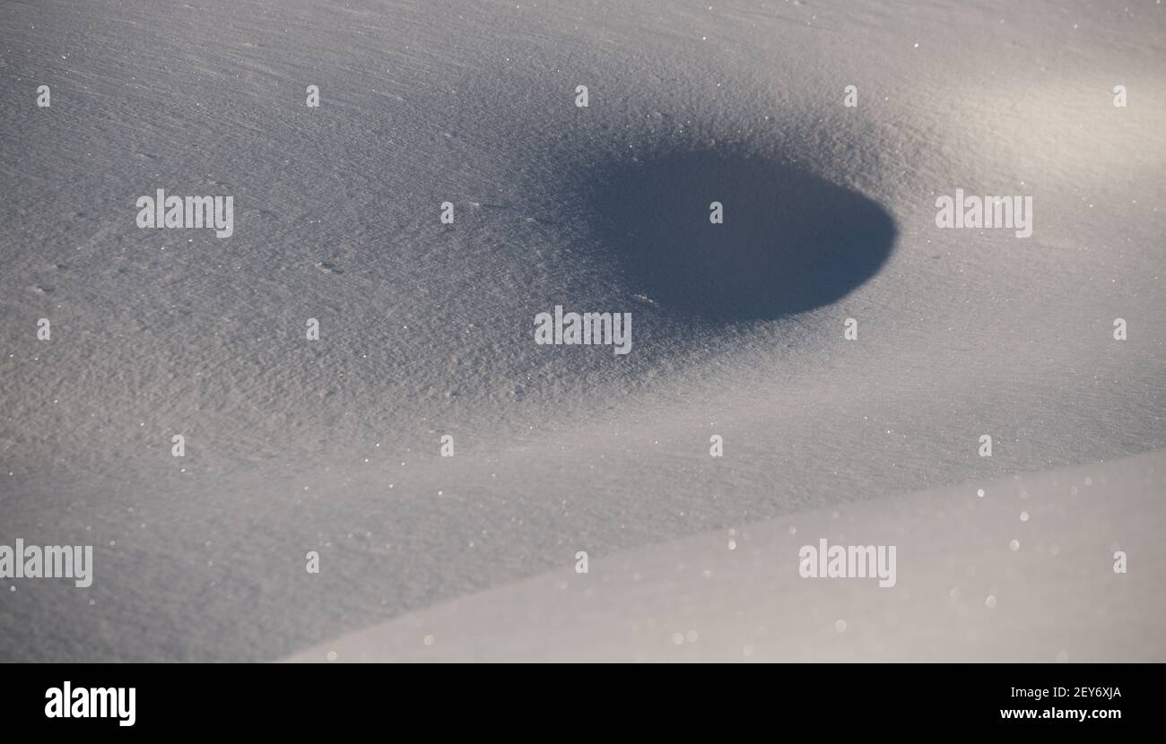 close up of mounds of snow in winter day time with sun casting shadows on curves of hills of snow smooth fresh snow peaceful tranquility feeling holes Stock Photo