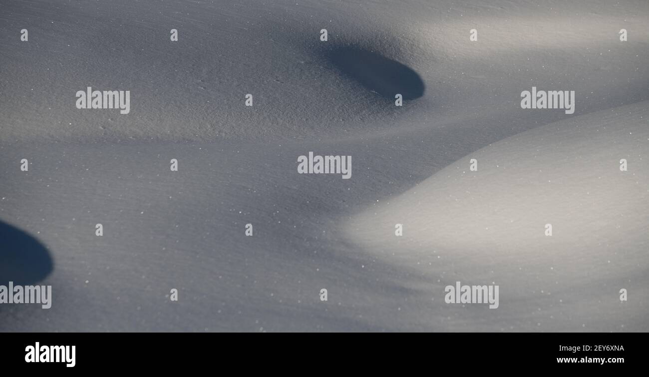 close up of mounds of snow in winter day time with sun casting shadows on curves of hills of snow smooth fresh snow peaceful tranquility feeling holes Stock Photo