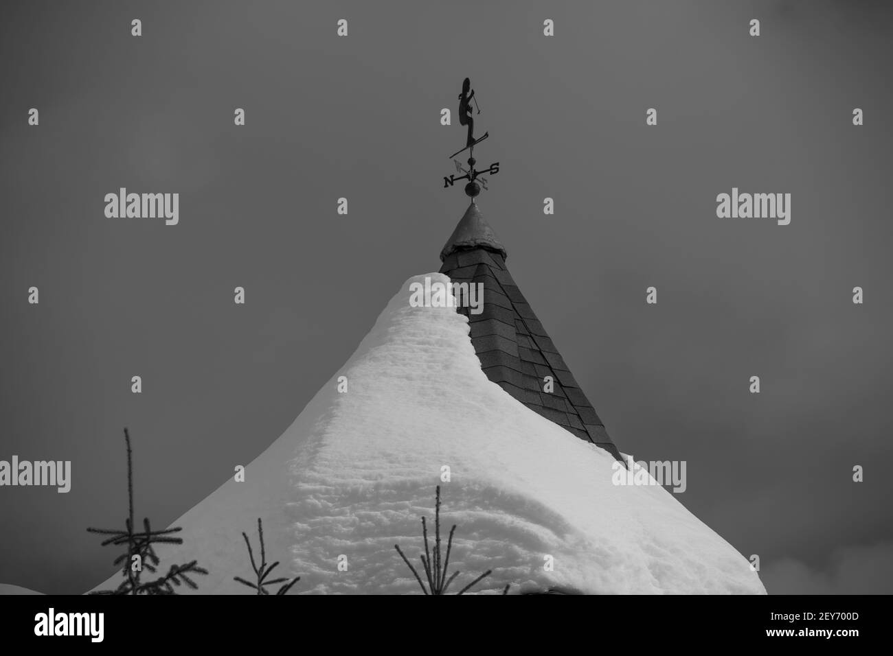 snow covered round dome roof of ski chalet at ski resort in British Columbia with a weather vane shaped like a skier wiht north east west and south Stock Photo
