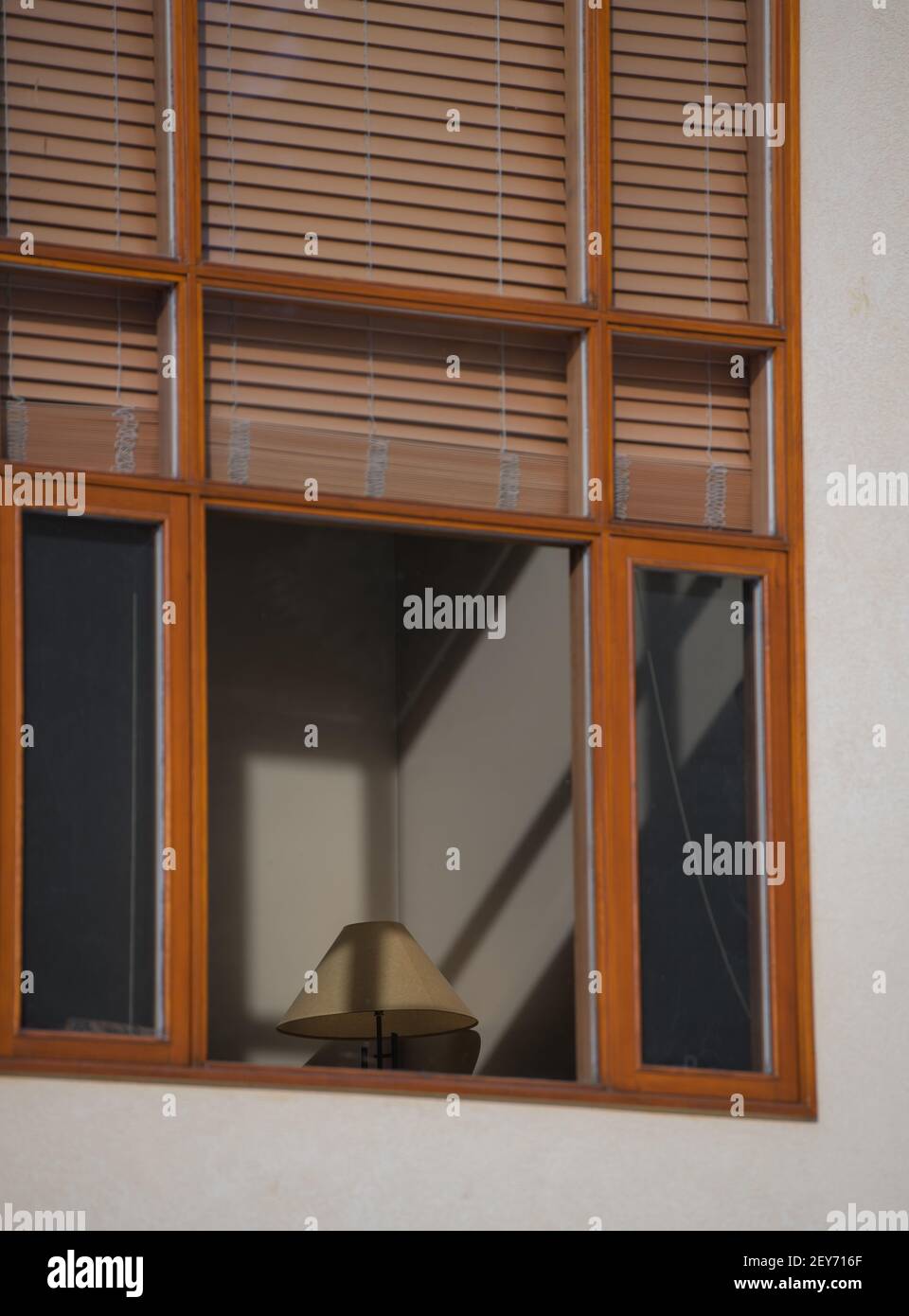 brown window blinds or shades blocking light coming through exterior wood framed home window light casting shadows on onterior wall sof home and lamp Stock Photo