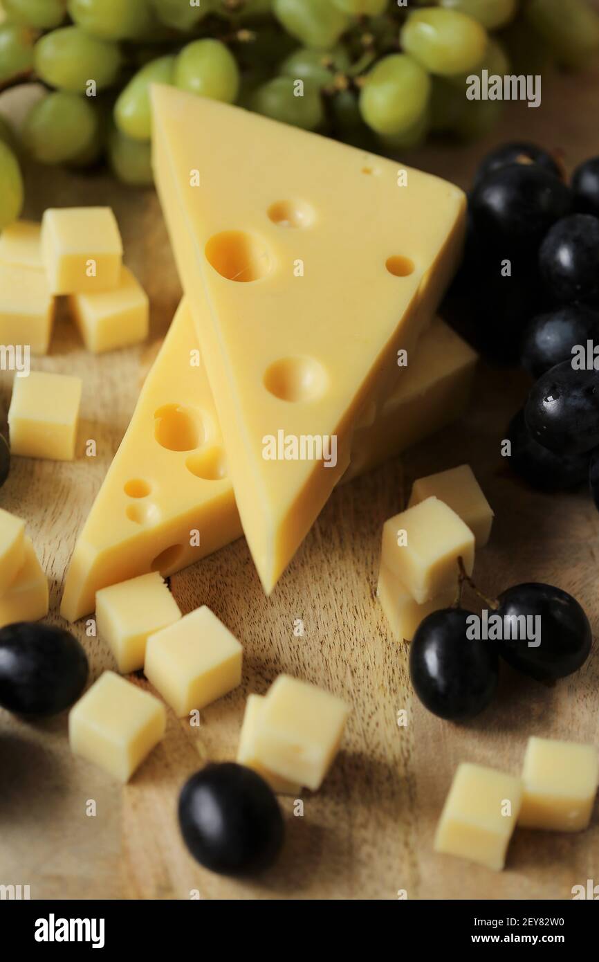 maasdamer cheese. Piece of cheese maasdam or maasdamer,green and black grapes brush on wooden board on brown background.Hard cheeses. Dairy products Stock Photo