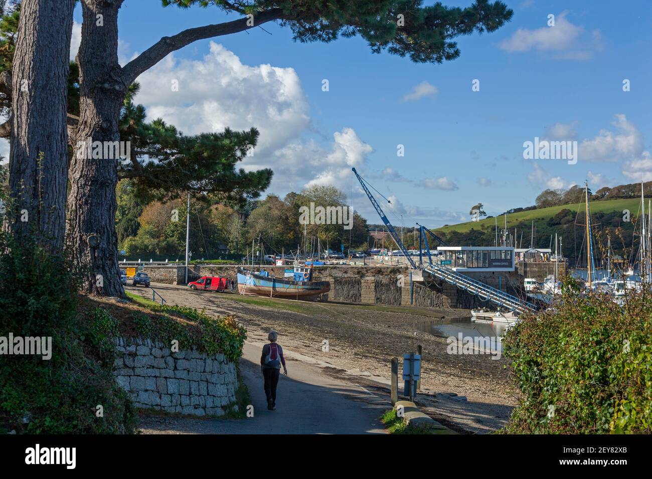 A walker on the coastal footpath from Penryn approaches Mylor Yatch Harbour near Falmouth in Cornwall at low tide. Stock Photo