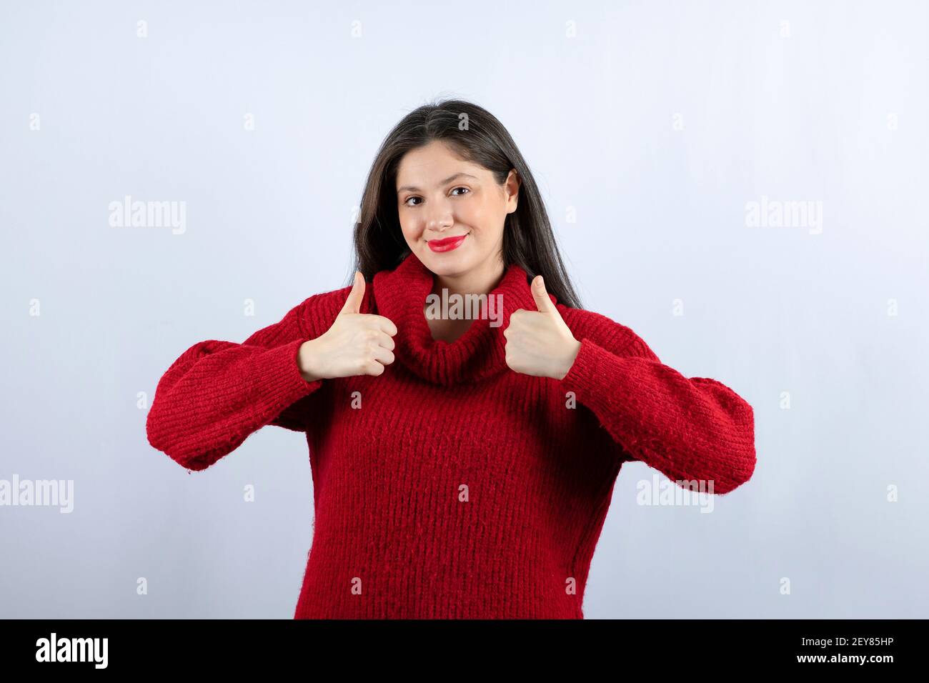 Photo of a pleased young woman in red sweater showing thumbs up Stock Photo