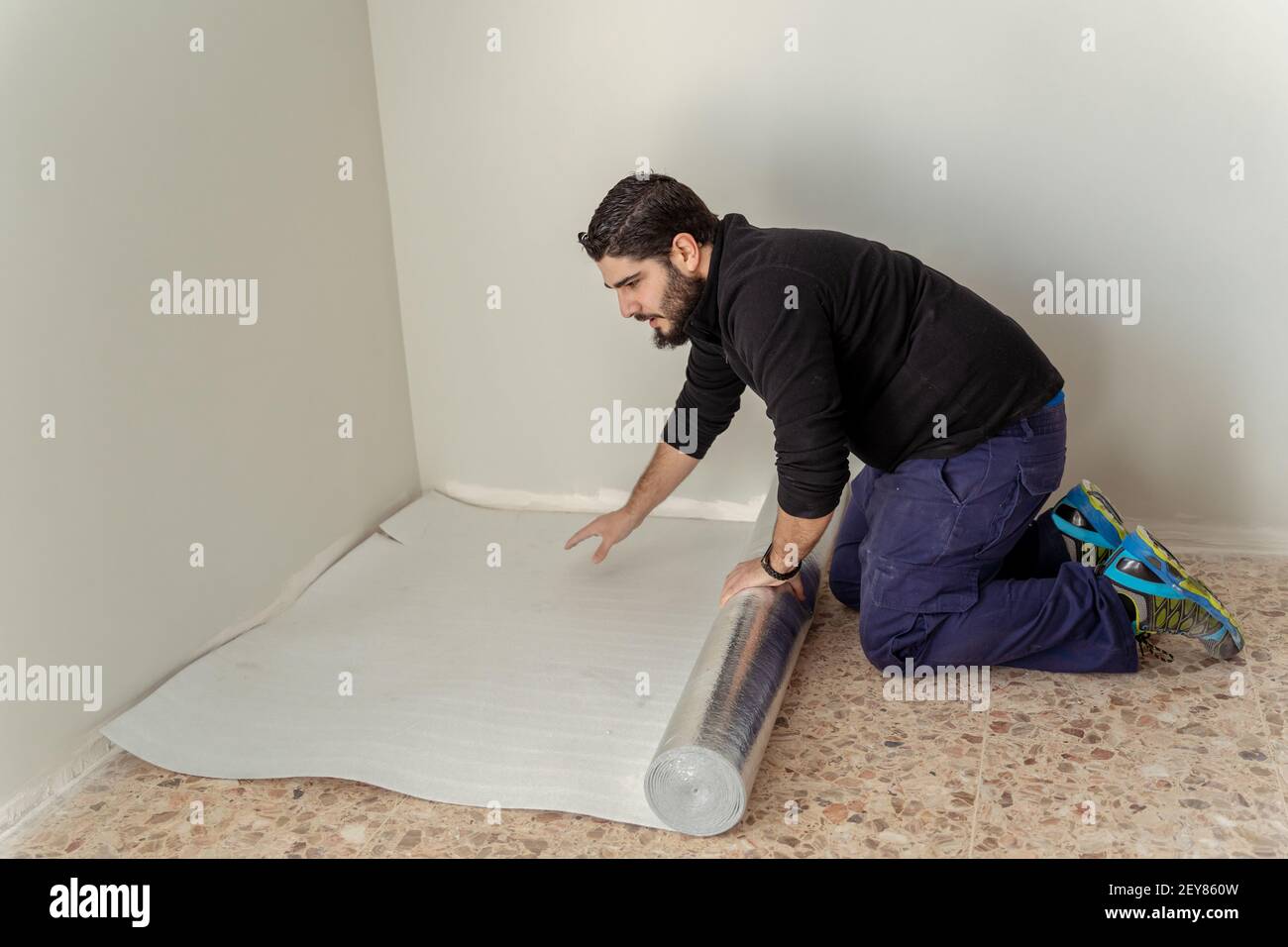 Builder man spreading the floor insulation to install the wooden floor Stock Photo