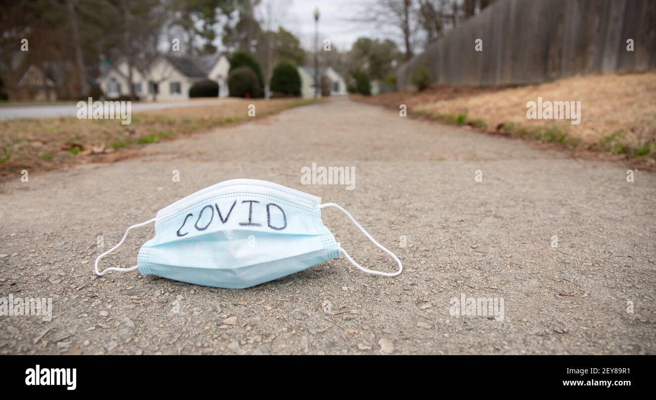 A mask with the word covid written on it laying on a community sidewalk. Stock Photo