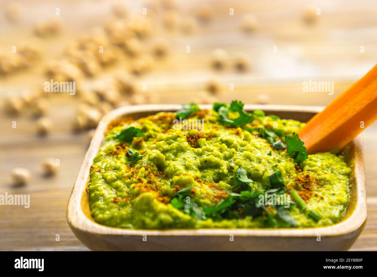 Homemade chickpea hummus with herbs in square bamboo wooden bowl, carrot stick Stock Photo