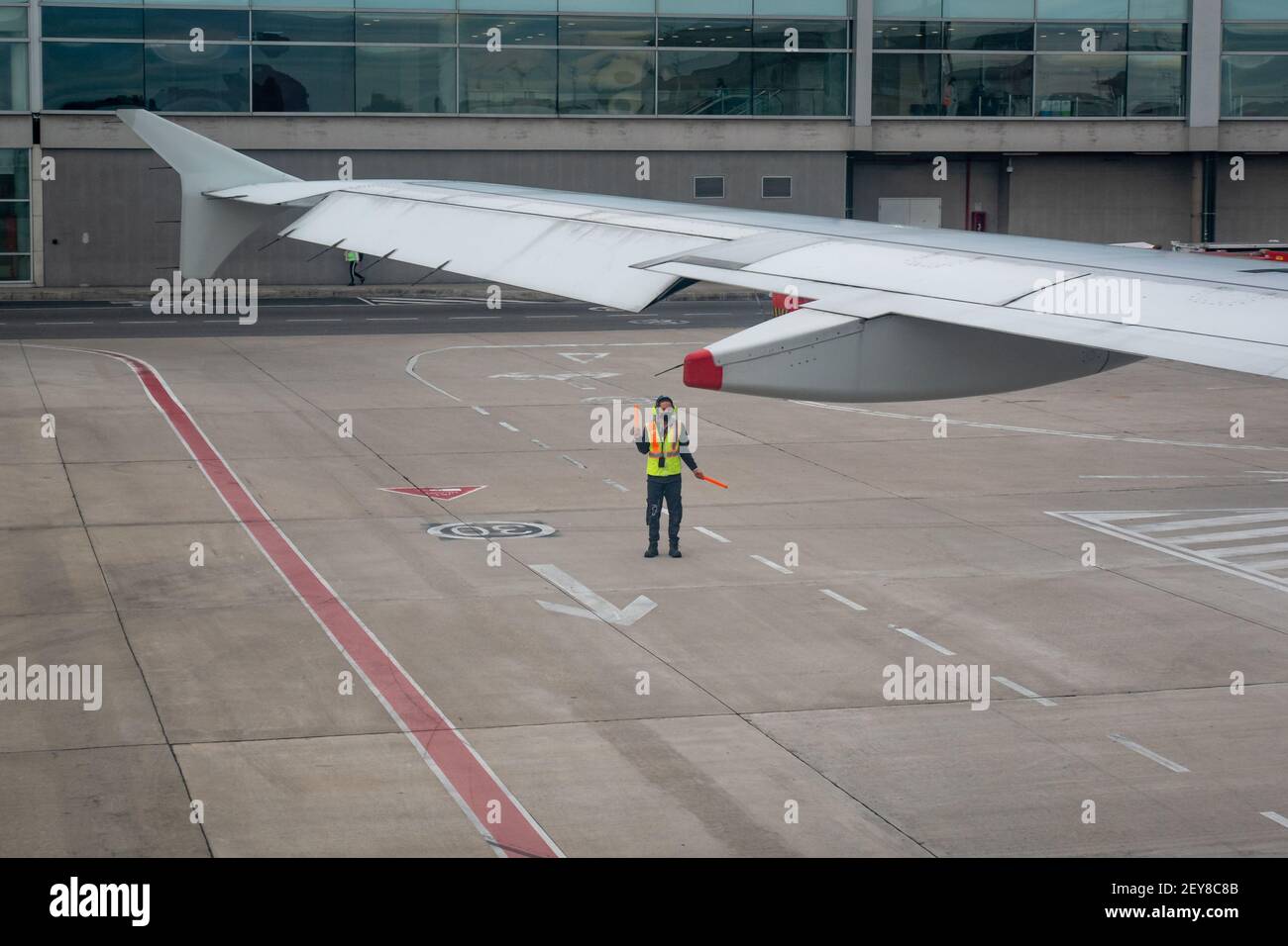 Bogota, Colombia - February 25 2021: Latin Man Wearing Mask, Yellow Vest Walks Down Runway with a Orange Cones to Indicate to Pilot when to Brake Stock Photo