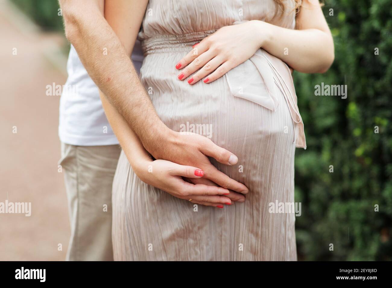 Man Hands Hug Pregnant Woman by Belly Closeup Photography. Staying Beautiful Pregnancy Girl Dressed in Dress. Future Parents and Childbirth Horizontal Stock Photo