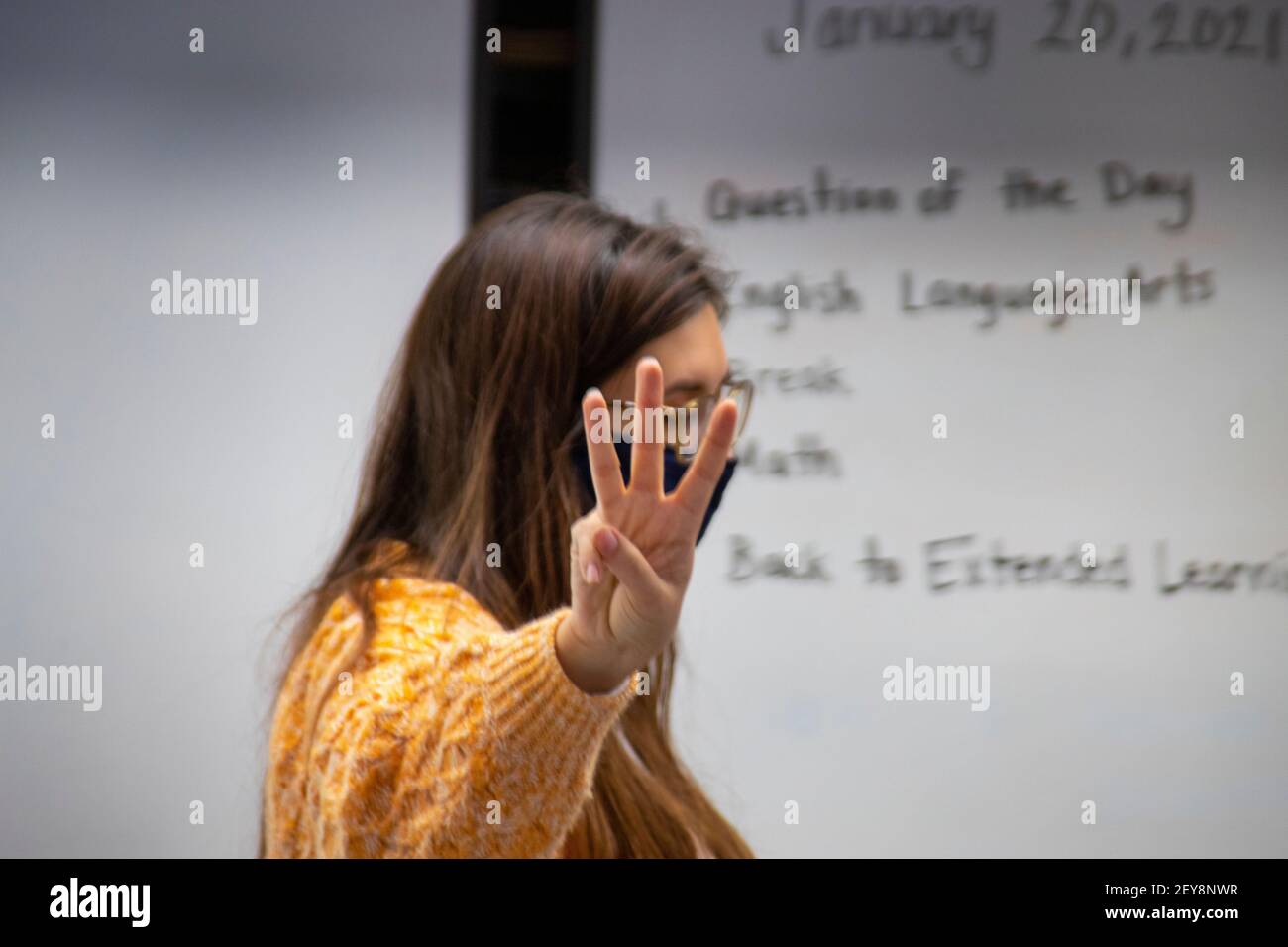 Holding up three fingers, a California elementary school teacher explains three syllable words to her third grade language arts students. Note face mask due to the coronavirus pandemic. Stock Photo
