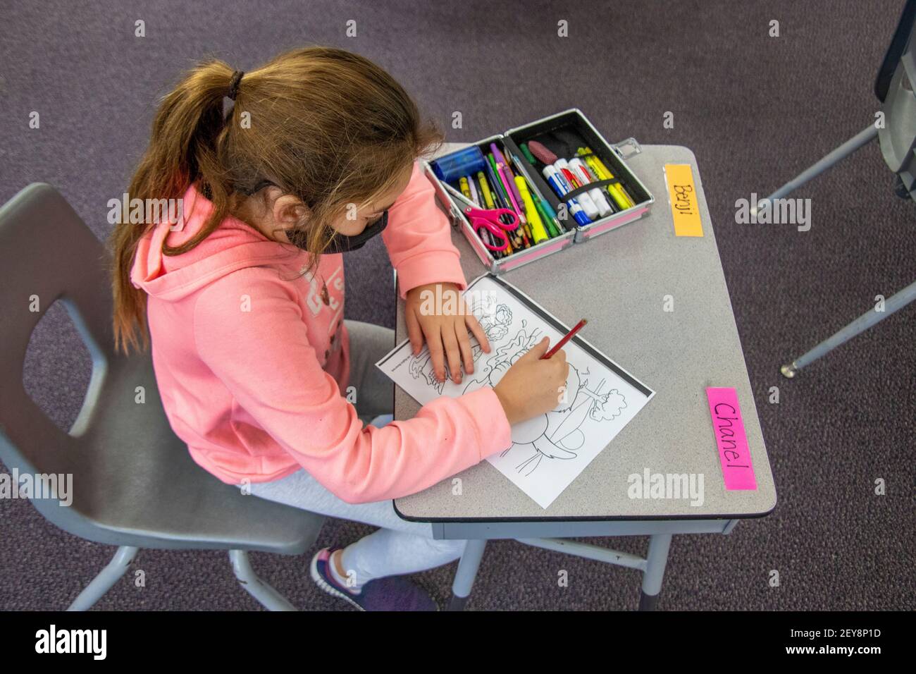 With her art supplies handy, a California elementary school student starts coloring in a friendly bear. Note face mask due to coronavirus pandemic. Stock Photo