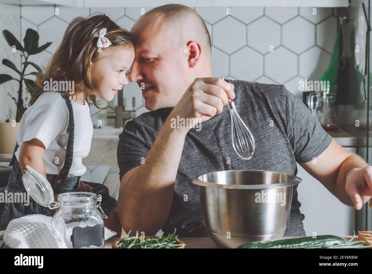 Father whips omelet with whisk, playing with daughter. Man doing chores. Stock Photo