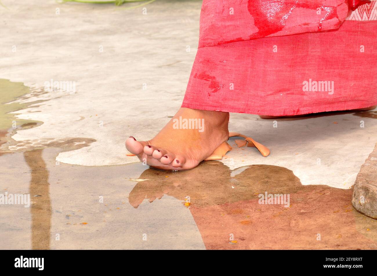 A barefoot woman breaking a clay dish using her foot in India Bengali