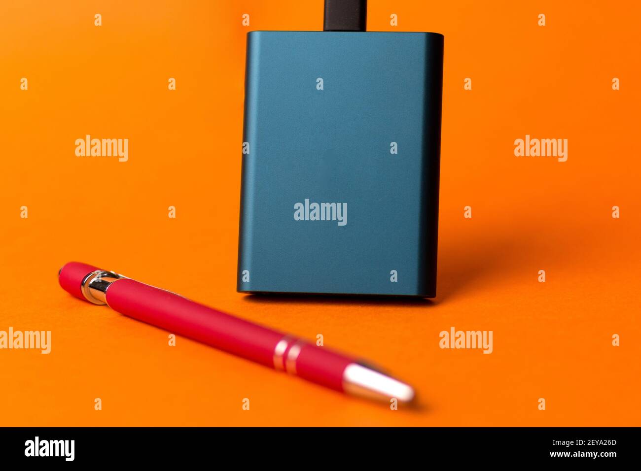 An external SSD disk and a red pen isolated on an orange background Stock Photo