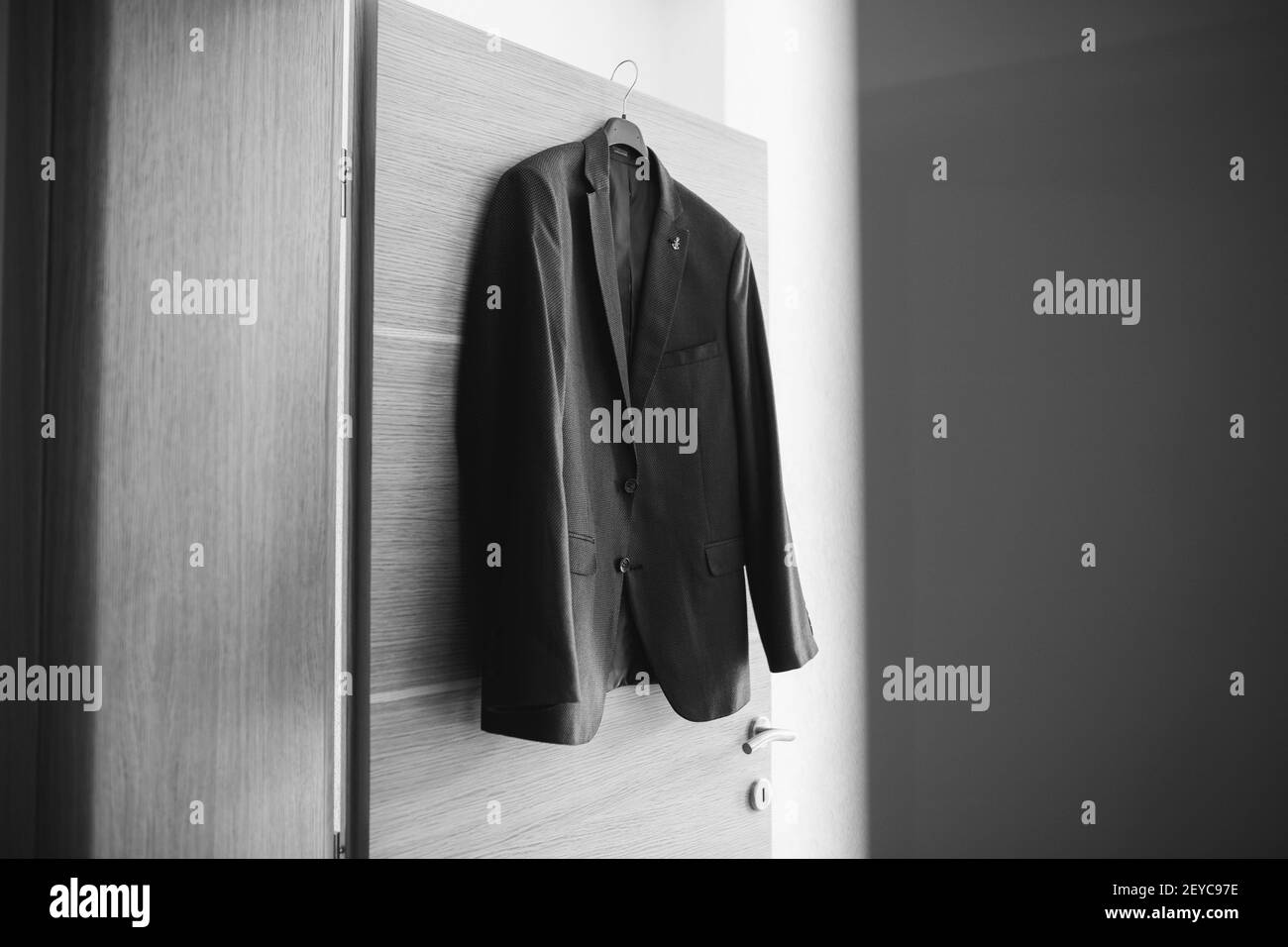 A grayscale closeup of the male's coat hanging on the wooden door Stock Photo
