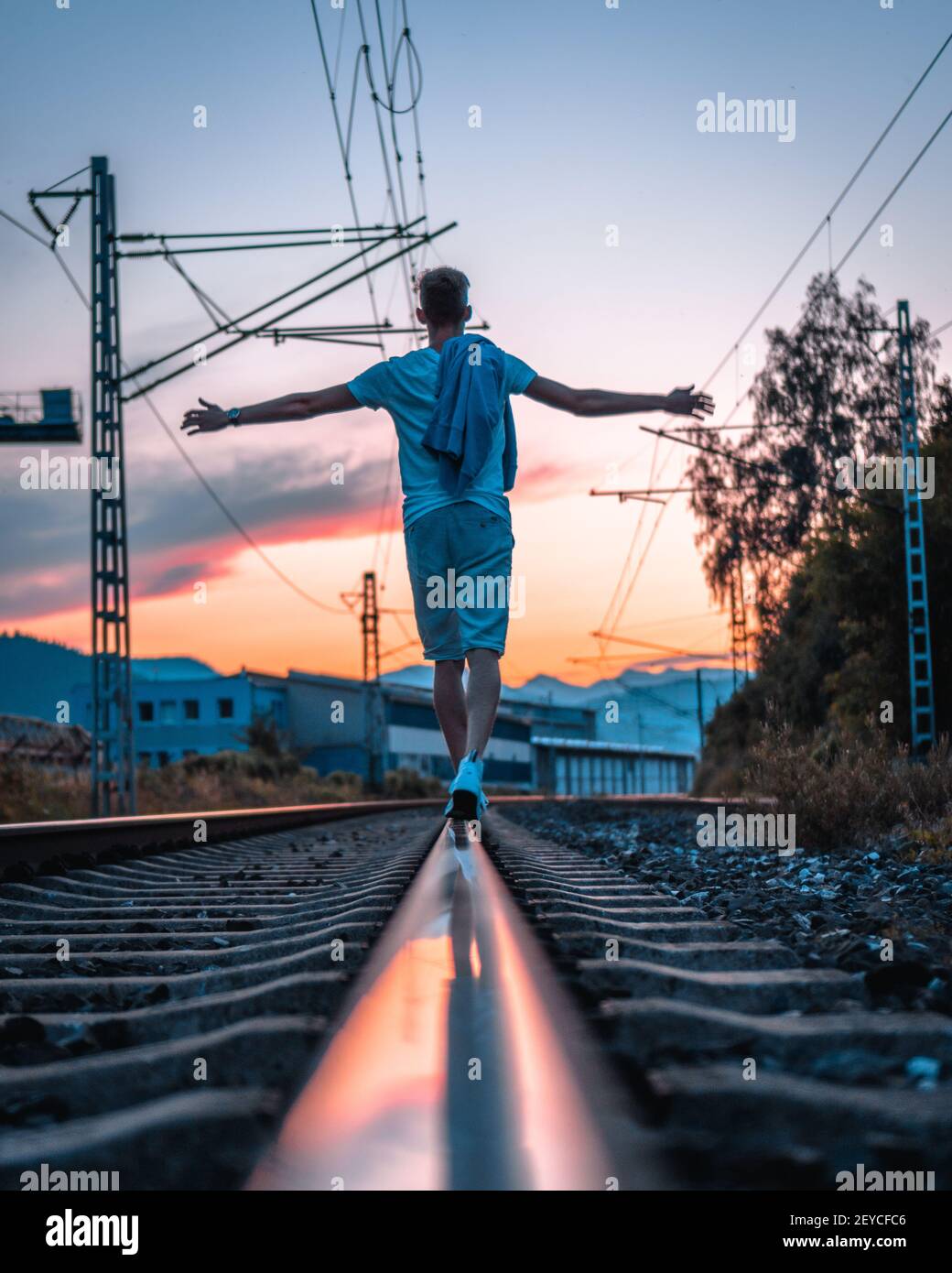 A back view of man balancing on the railway track with a golden sunset ...