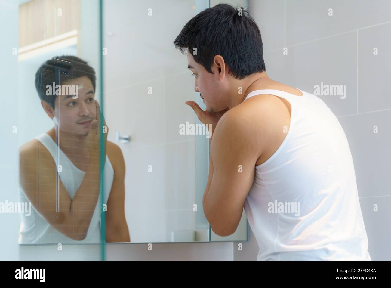 Asian man are applying moisturizer facial cream to his face after bathing and getting ready to work in the bathroom in the house. Stock Photo