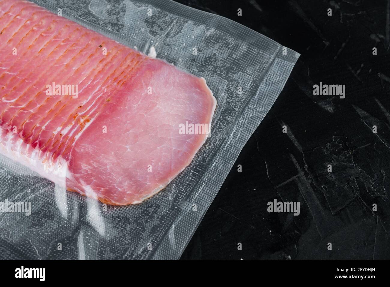 Cured meat pork ham set, vacuum packed, on black stone background, with