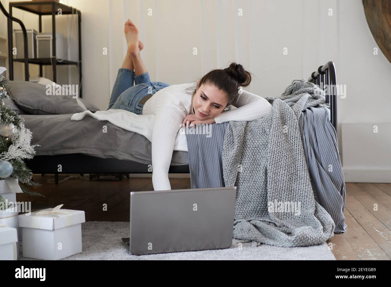 Young beautiful bruenette woman in cozy sweater in bed at home working on laptop Stock Photo