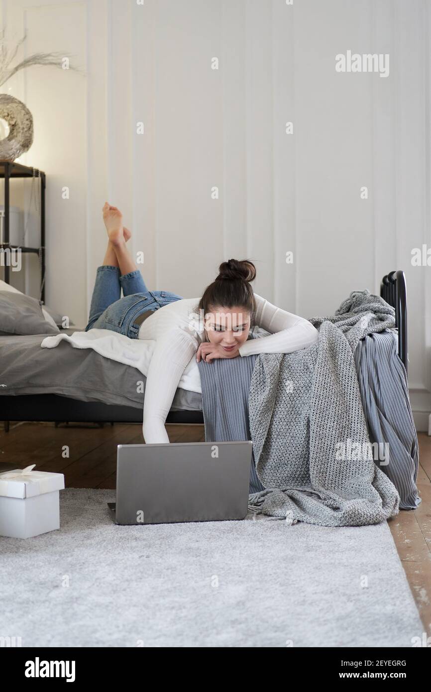 Young beautiful bruenette woman in cozy sweater in bed at home working on laptop Stock Photo