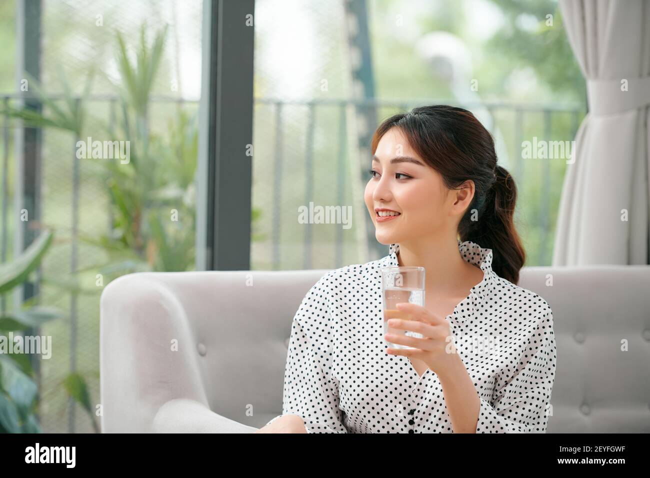 Pretty asian woman drinking water on couch at home in the living room