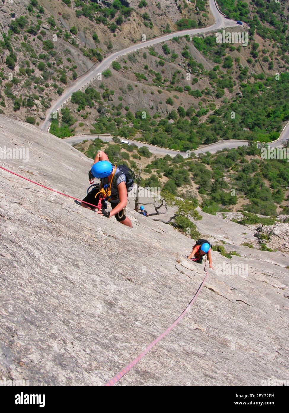Two climbers in gear climb the cliff, top view, view of the valley and the serpentine road Stock Photo