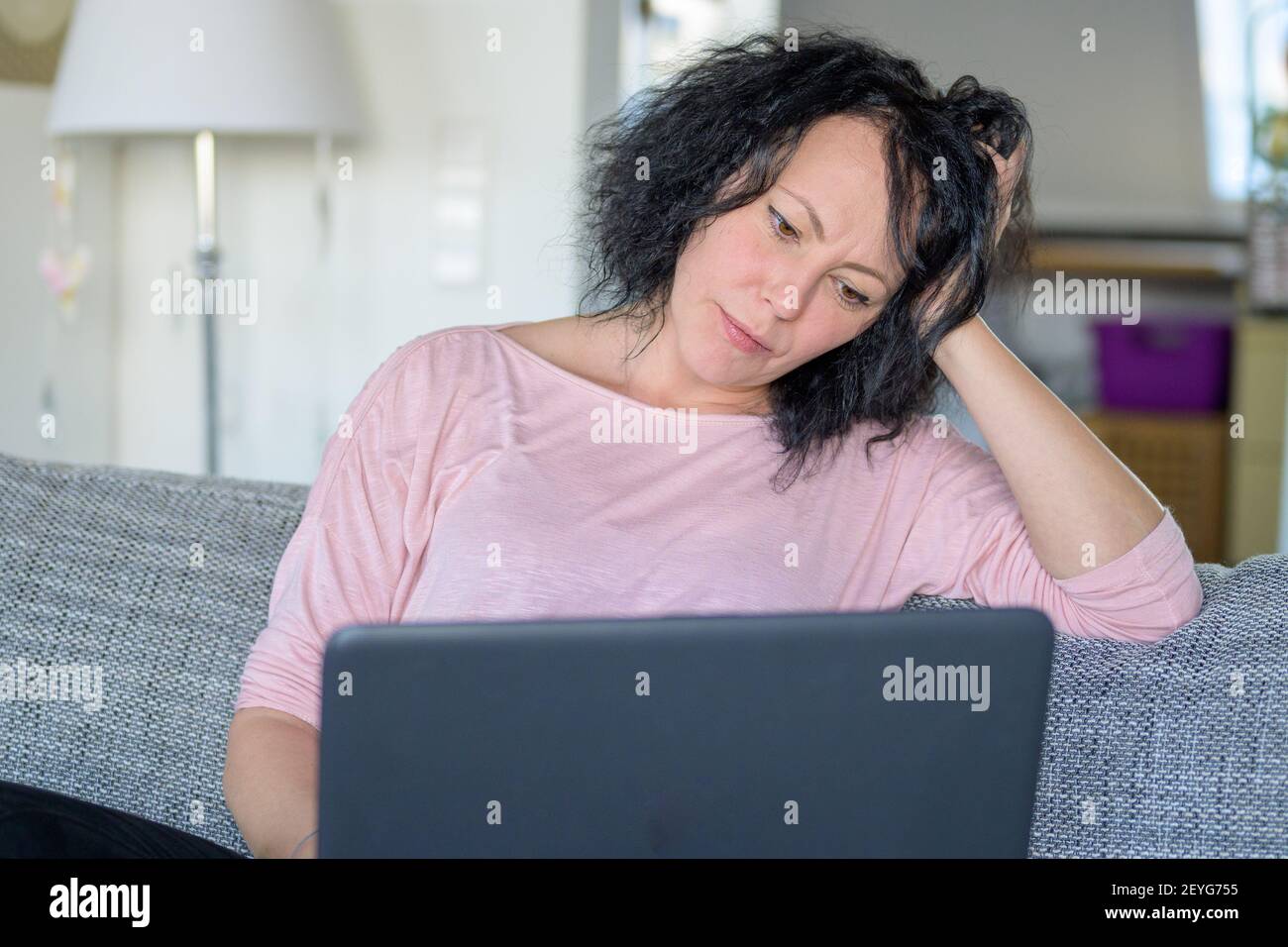 Woman sitting pensively at her computer on the couch Stock Photo