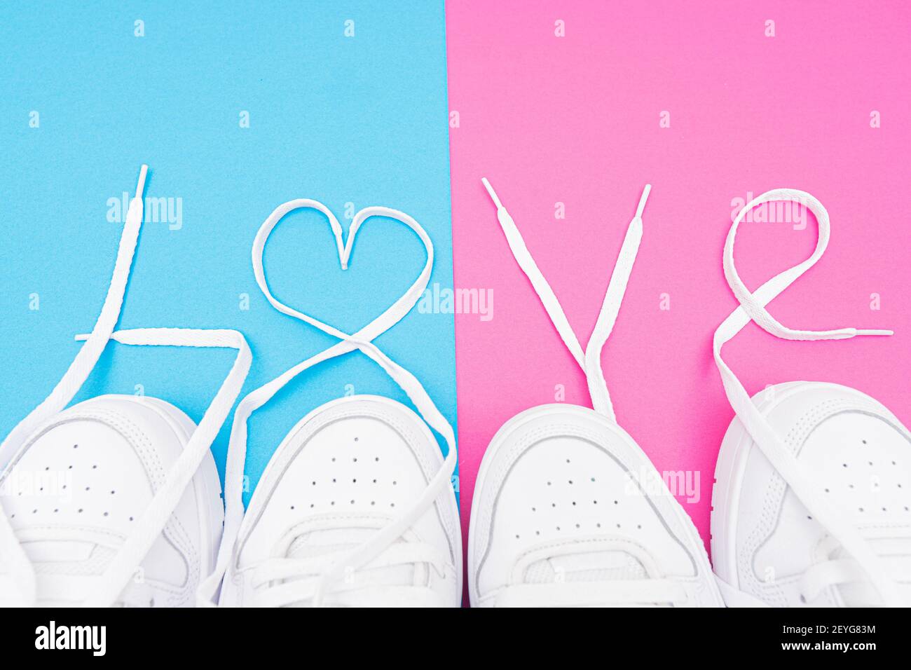 Matching white sneakers with the lettering LOVE made of the laces on a contrast blue and pink background. Matching outfits for couples idea. Stock Photo