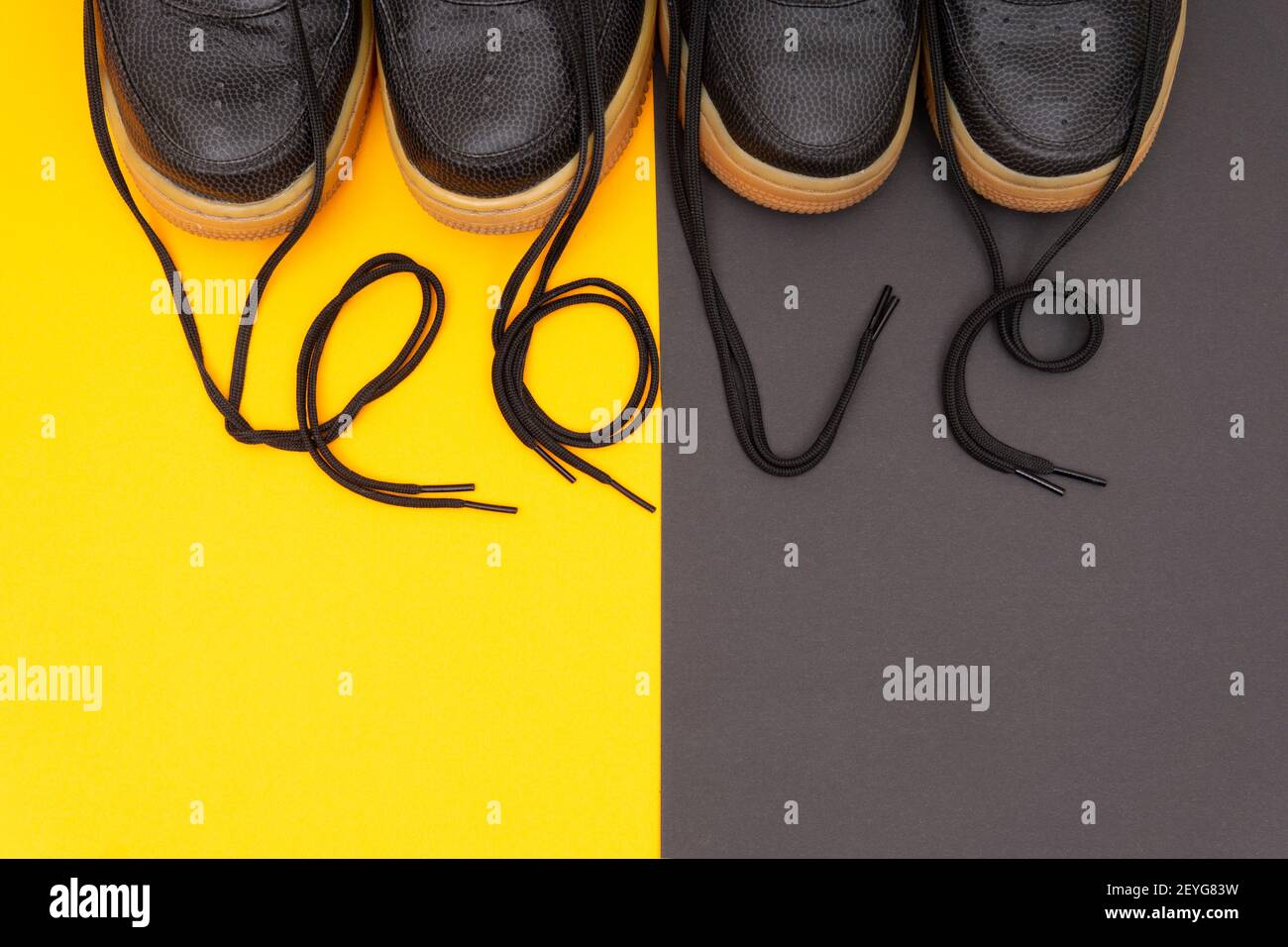 Matching leather sneakers with the lettering LOVE made of the laces on a contrast yellow and brown background. Romantic concept of wearing matching ou Stock Photo